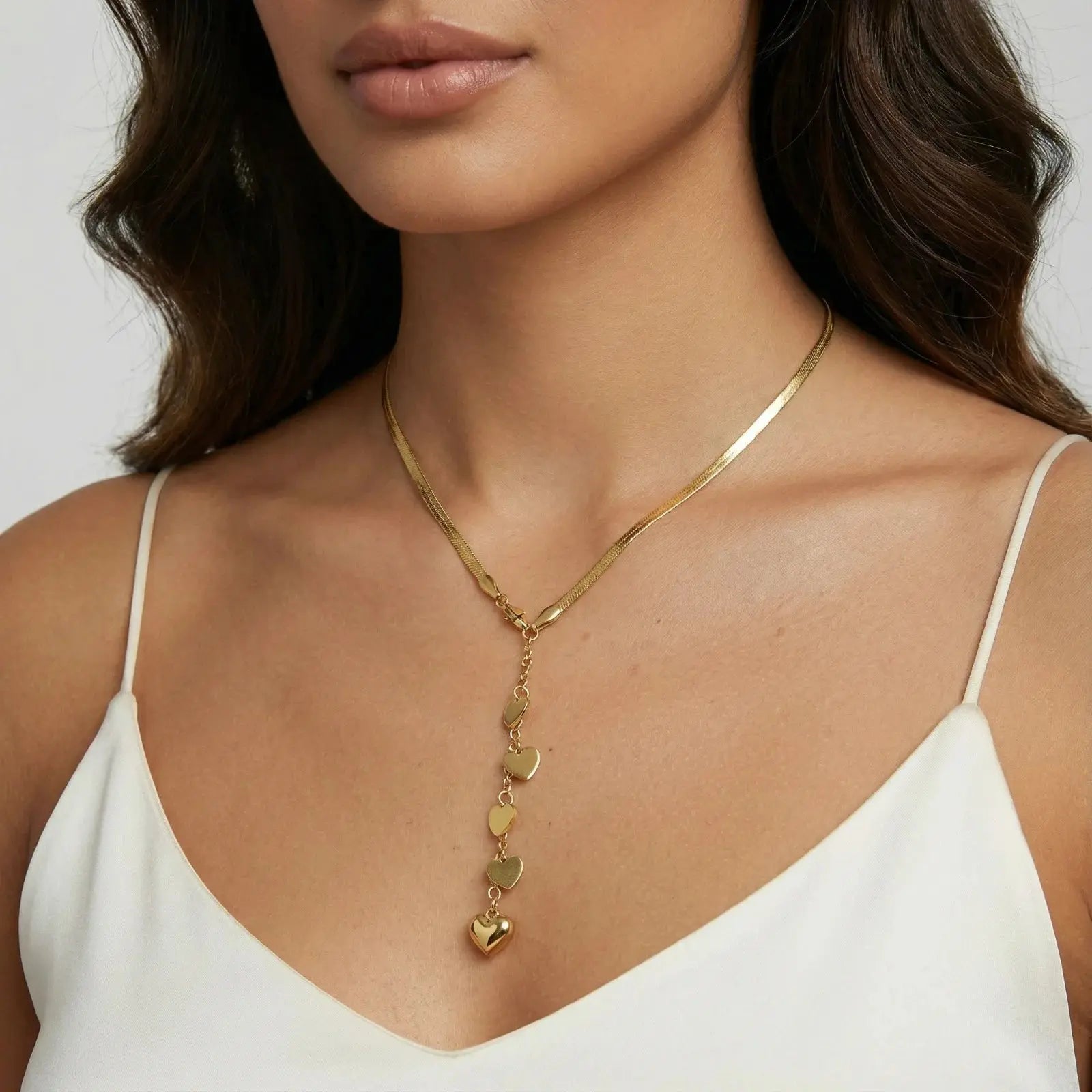 Woman wearing a gold Y necklace with cascading heart charms, styled with a white top.