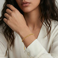 Woman wearing a gold bracelet on a neutral background