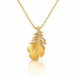 A gold pendant necklace featuring a textured leaf design adorned with small clear stones, suspended from a gold ball chain on a white background with a soft reflection below.