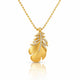 A gold pendant necklace featuring a textured leaf design adorned with small clear stones, suspended from a gold ball chain on a white background with a soft reflection below.