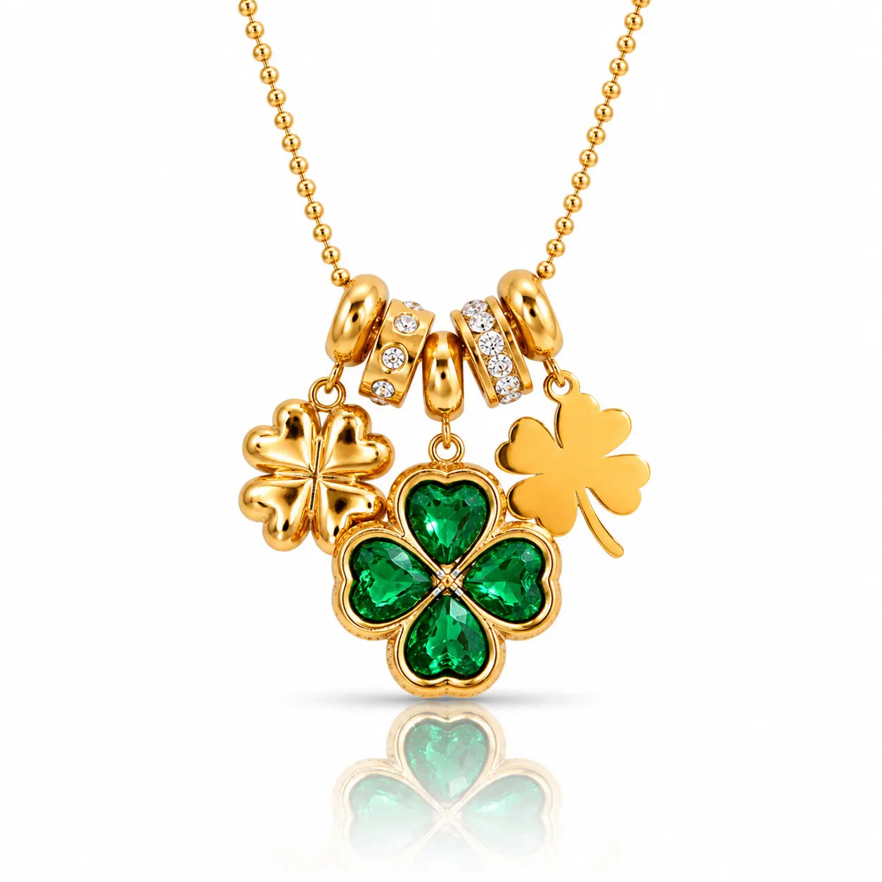 A gold St. Patrick's Day necklace featuring three shamrock charms: one large green four-leaf clover with emerald-cut stones, one solid gold shamrock, and one small gold shamrock with clear stones, on a gold ball chain.
