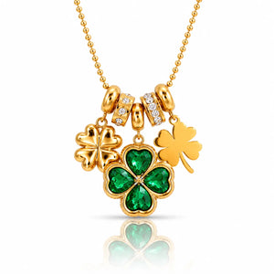 A gold St. Patrick's Day necklace featuring three shamrock charms: one large green four-leaf clover with emerald-cut stones, one solid gold shamrock, and one small gold shamrock with clear stones, on a gold ball chain.