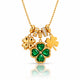 A gold St. Patrick's Day necklace featuring three shamrock charms: one large green four-leaf clover with emerald-cut stones, one solid gold shamrock, and one small gold shamrock with clear stones, on a gold ball chain.
