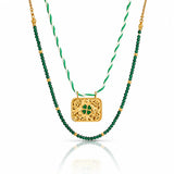 A double-strand St. Patrick's Day necklace featuring a gold filigree clover pendant and a green beaded strand layered over a white and green twisted cord chain.