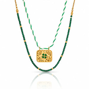 A double-strand St. Patrick's Day necklace featuring a gold filigree clover pendant and a green beaded strand layered over a white and green twisted cord chain.