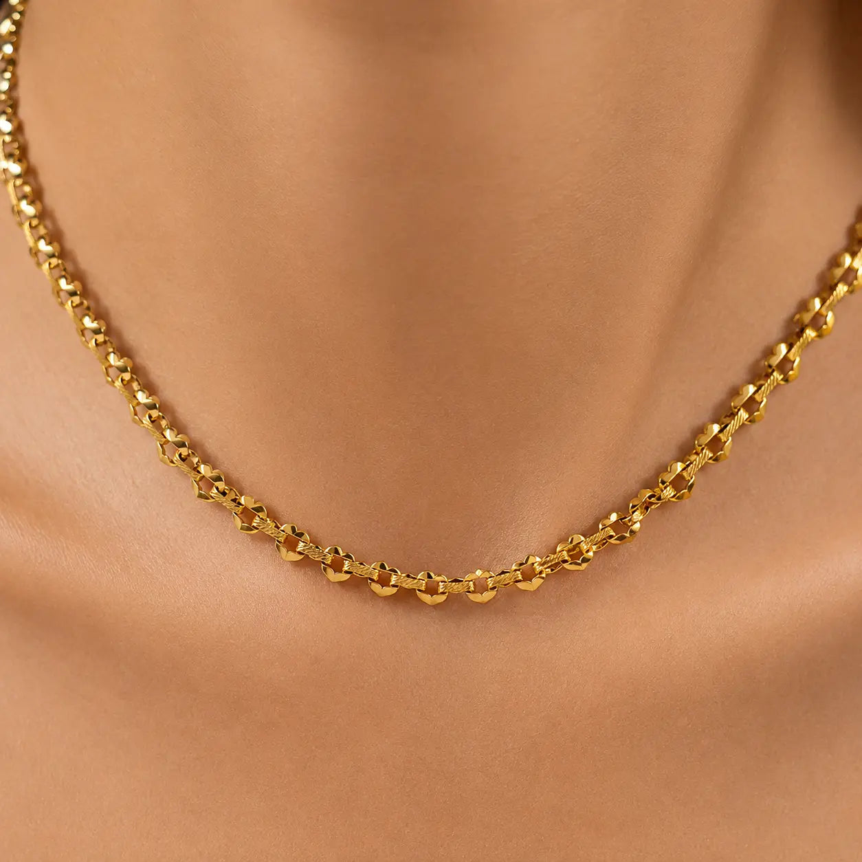 A close-up of a gold chain necklace worn on a model's neck, showing the detailed links of the chain against warm skin tones.