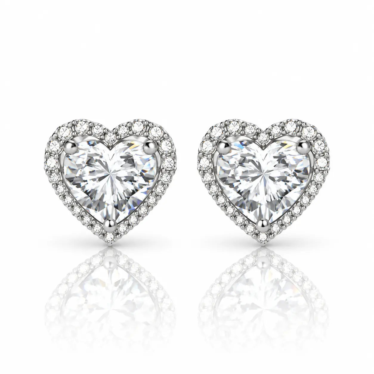 A pair of heart-shaped stud earrings featuring large clear heart-cut center stones surrounded by a halo of smaller clear stones, set in a silver-toned metal on a white background with a soft reflection below.