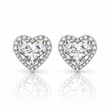 A pair of heart-shaped stud earrings featuring large clear heart-cut center stones surrounded by a halo of smaller clear stones, set in a silver-toned metal on a white background with a soft reflection below.