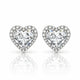 A pair of heart-shaped stud earrings featuring large clear heart-cut center stones surrounded by a halo of smaller clear stones, set in a silver-toned metal on a white background with a soft reflection below.