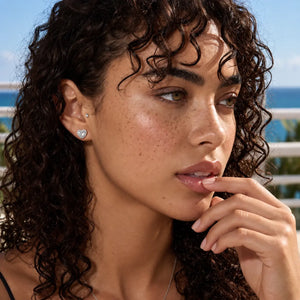 A close-up lifestyle shot of a woman with curly dark hair wearing a small silver heart-shaped stud earring. The earring features a clear heart-shaped gemstone, which does not contribute to the color mapping according to the rules.
