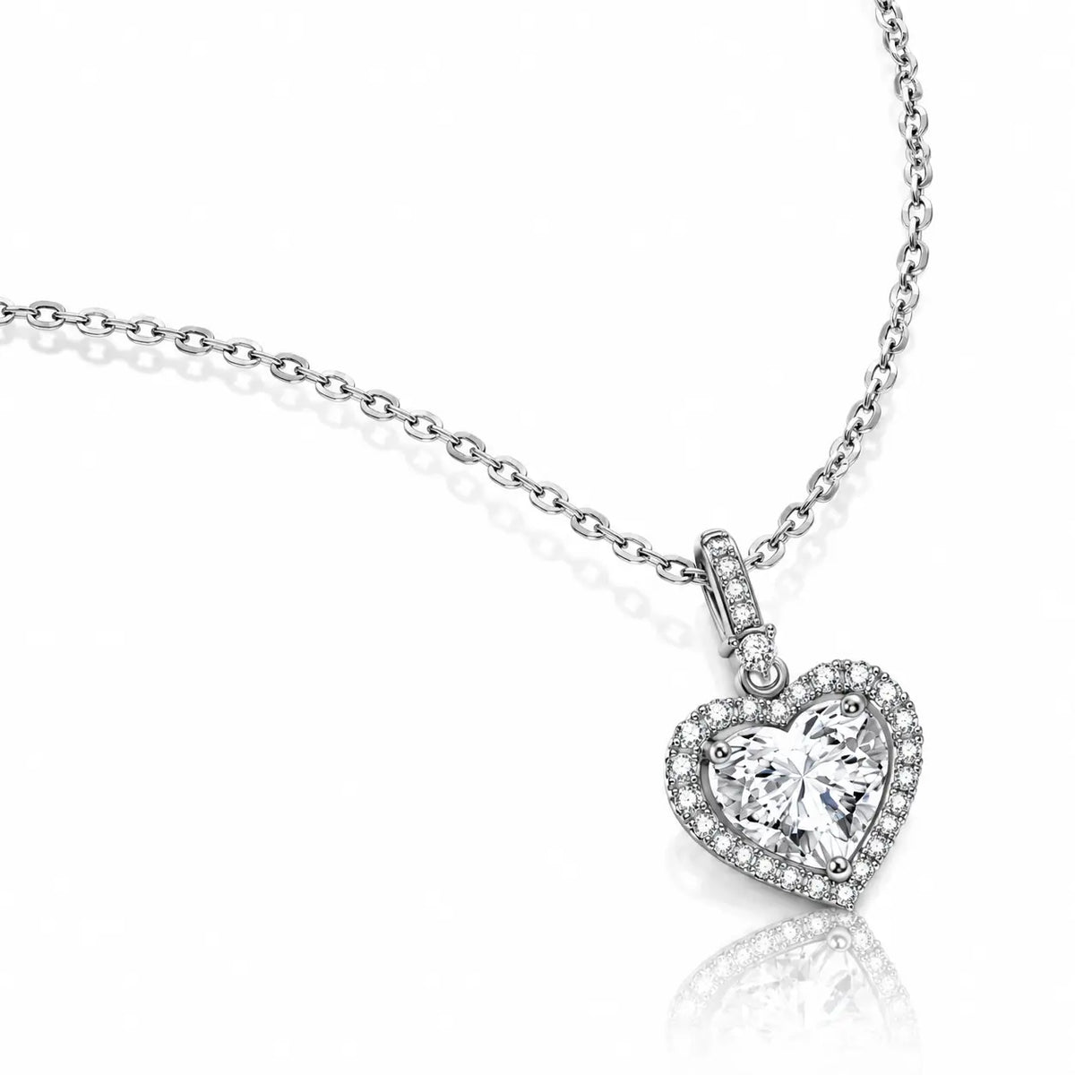 A silver heart-shaped pendant necklace with a halo of small clear stones surrounding a larger central clear heart-shaped stone, shown on a white background with a soft reflection.