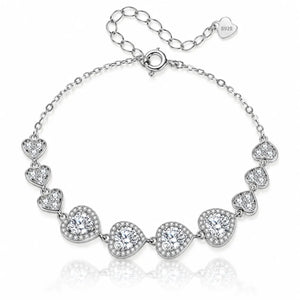 A silver-tone chain bracelet featuring seven heart-shaped settings, each adorned with clear stones, displayed on a clean white background with a soft reflection.