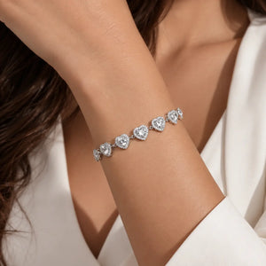 A close-up of a woman's wrist wearing a delicate silver bracelet with five heart-shaped pavé diamond clusters, styled with a white top.