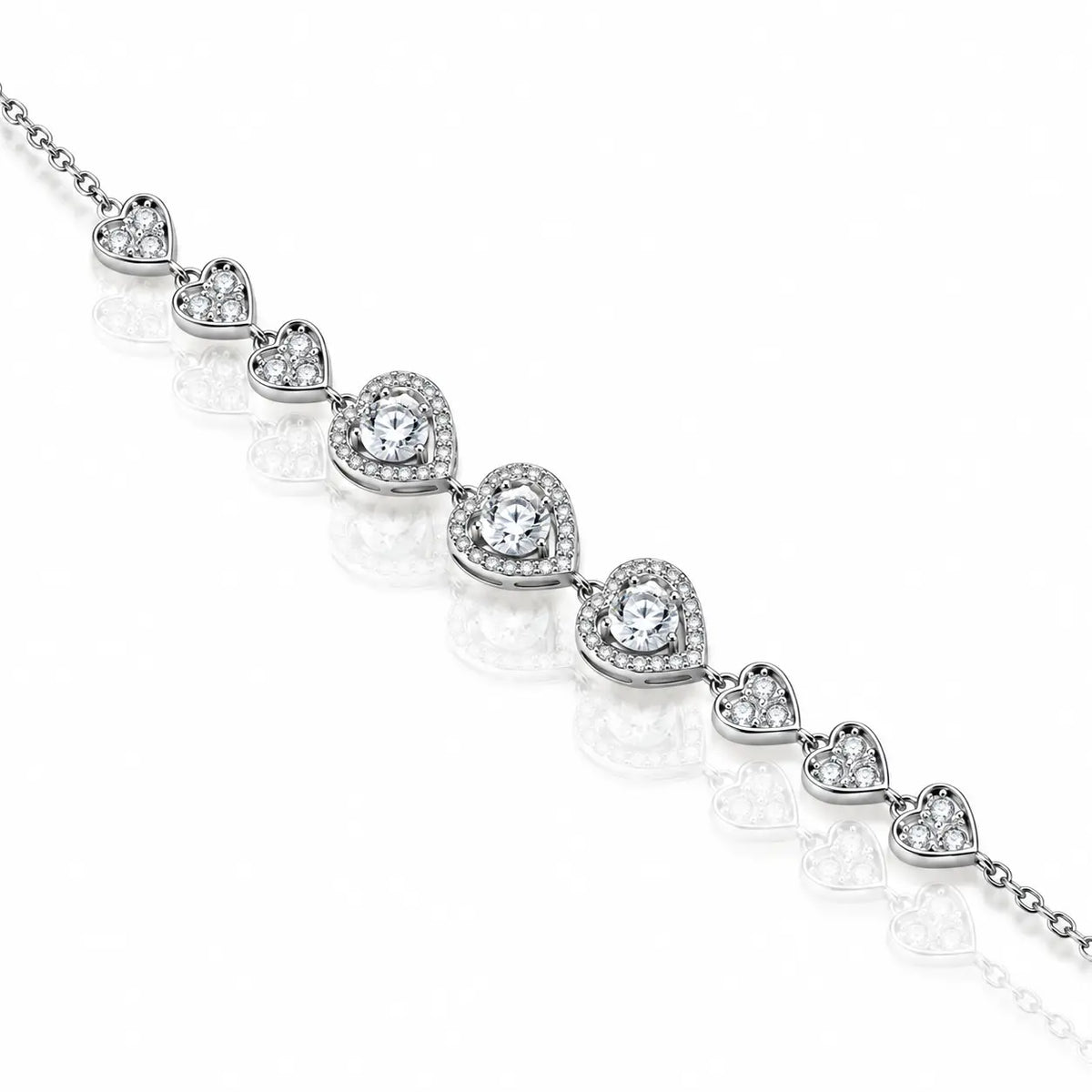 A silver-toned heart-link bracelet featuring clear heart-shaped gemstones surrounded by smaller pavé accents, displayed diagonally on a reflective white surface.