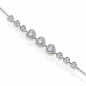 A silver-toned heart-link bracelet featuring clear heart-shaped gemstones surrounded by smaller pavé accents, displayed diagonally on a reflective white surface.