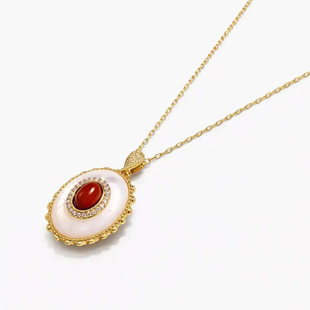 Gold oval cameo pendant necklace with red gemstone and clear crystal accents on white background