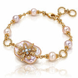 A gold chain bracelet featuring baroque-style pinkish pearl beads and a large central iridescent pearl pendant with a gold floral filigree setting and small clear stones, shown on a white reflective background.