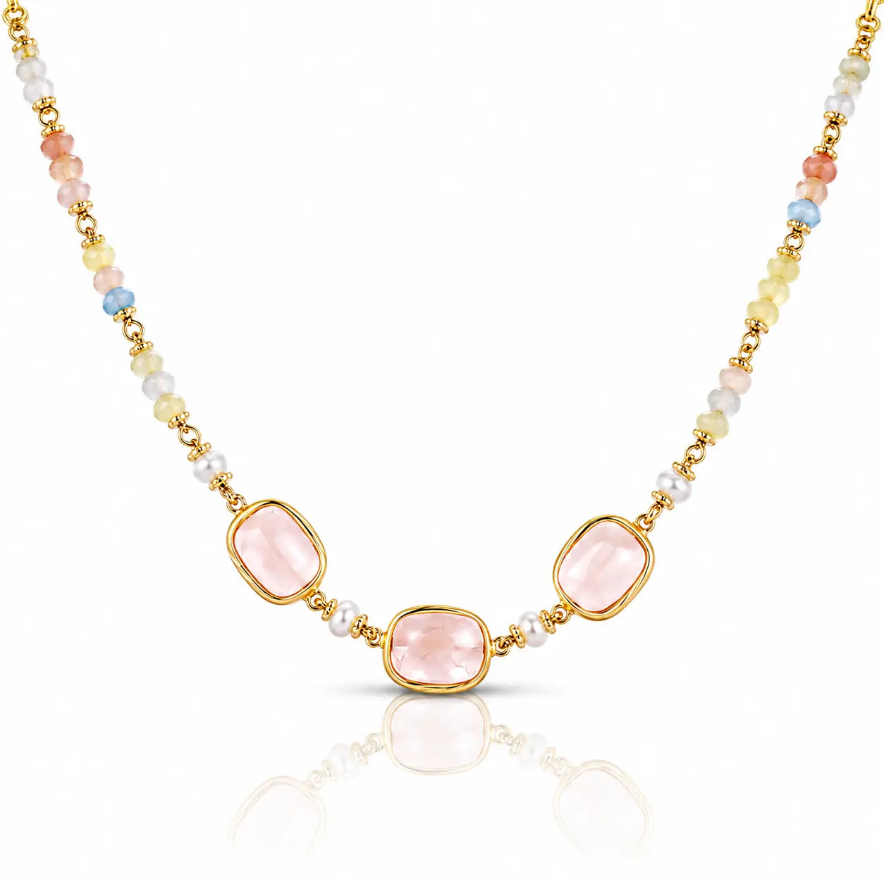 A gold-tone beaded necklace featuring three central light pink rectangular gemstones, flanked by small white pearls and multicolored beads in pastel shades of yellow, blue, and peach, set against a clean white background with a soft reflection below.