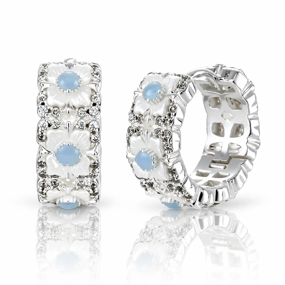 A pair of silver-toned hoop earrings with white floral enamel details, clear rhinestone accents, and light blue oval gemstones, displayed on a reflective white surface.