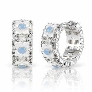 A pair of silver-toned hoop earrings with white floral enamel details, clear rhinestone accents, and light blue oval gemstones, displayed on a reflective white surface.