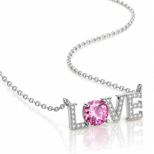 A silver-tone necklace featuring a 'LOVE' word pendant, where the letter 'O' is replaced by a round pink gemstone, set against a clean white background with a soft reflection.