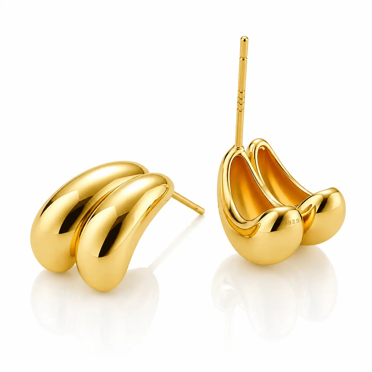 A pair of polished yellow gold earrings shaped like stylized, curved bean pods, shown on a clean white reflective surface. One earring is displayed from the front showing its smooth, glossy bean-like form, and the other is turned to show the post and backing.