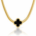 A gold chain necklace featuring a black four-leaf clover pendant with a textured gold border, displayed on a clean white background with a soft reflection below.