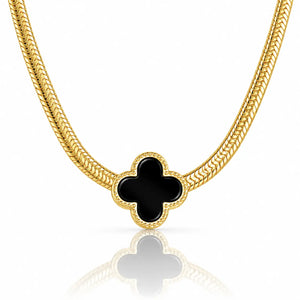 A gold chain necklace featuring a black four-leaf clover pendant with a textured gold border, displayed on a clean white background with a soft reflection below.