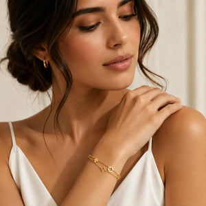 A woman wearing a delicate gold bracelet with a small star and flower motif on her wrist, paired with a white satin top against a soft beige background.