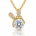 A gold pendant necklace featuring a bunny-shaped charm with a large round clear center stone and smaller clear stones along the ears and bow, shown on a white background with a soft reflection below.