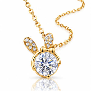 Gold bunny pendant necklace with a large round clear center stone and two small wing-shaped stones, shown on a white background with a reflection below.