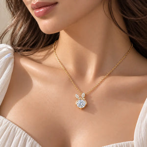 A close-up lifestyle shot of a model wearing a delicate gold chain necklace with a bow-shaped pendant adorned with small white pearls and a central clear round gemstone.