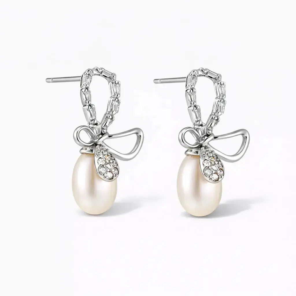 Silver bow earrings with pearl drops and crystal accents on a white background