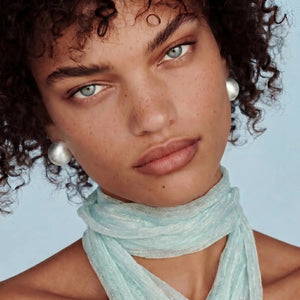 Woman wearing a light blue scarf with pearl earrings against a light blue background