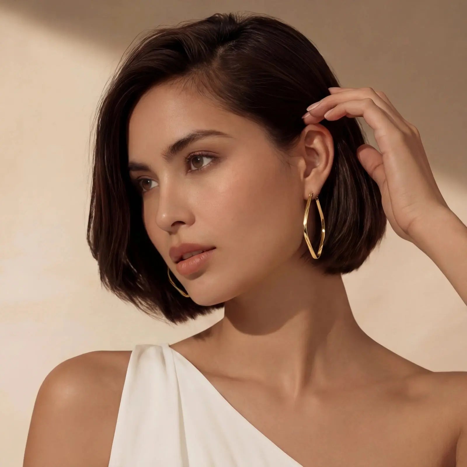 Woman wearing gold hoop earrings against a beige background