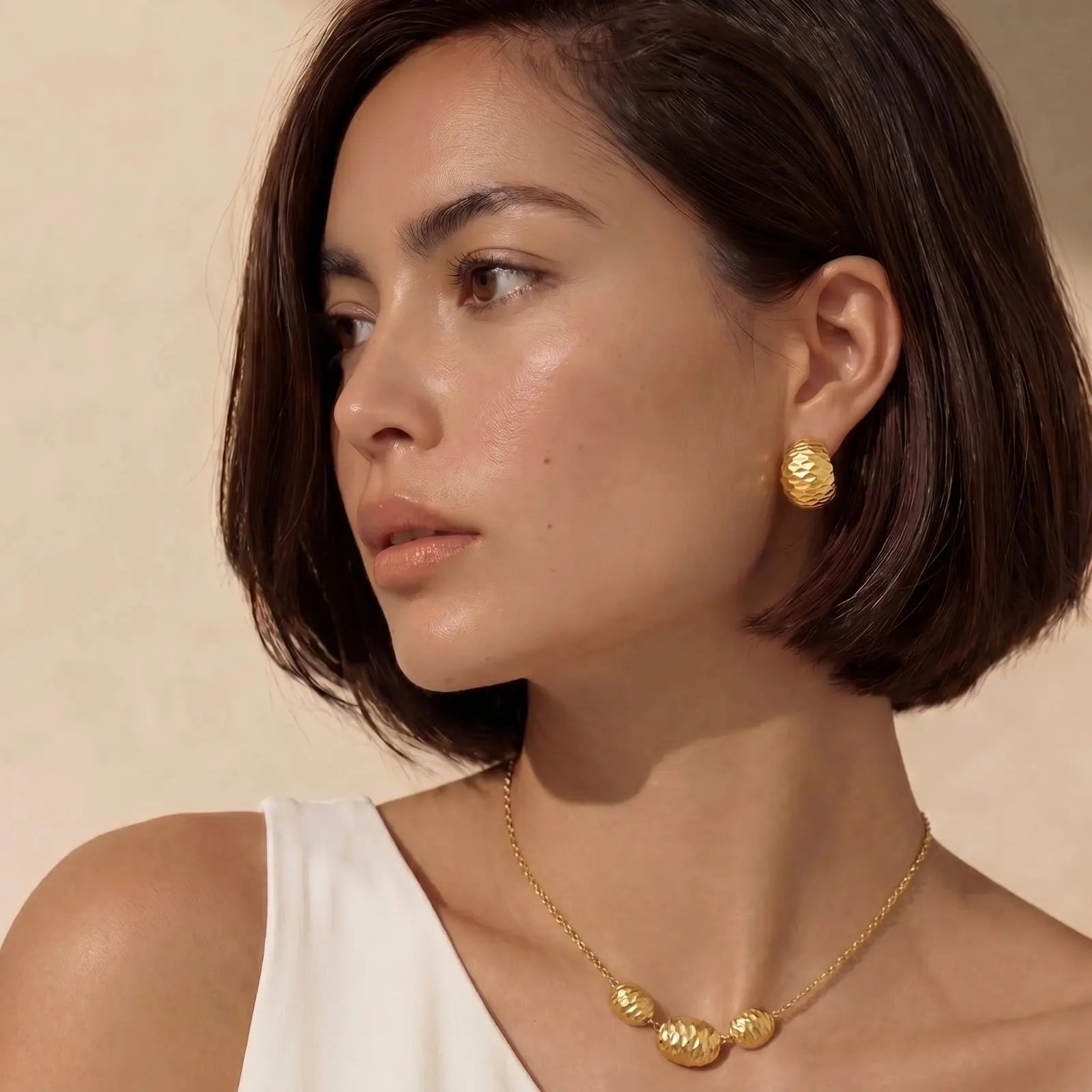 Woman wearing gold earrings and necklace against a beige background