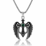 A silver-toned angel wing pendant necklace with a central green gemstone and black accents, suspended from a silver chain on a white background with a reflection below.