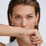 Close-up of a woman wearing gold earrings and a bracelet on a white background