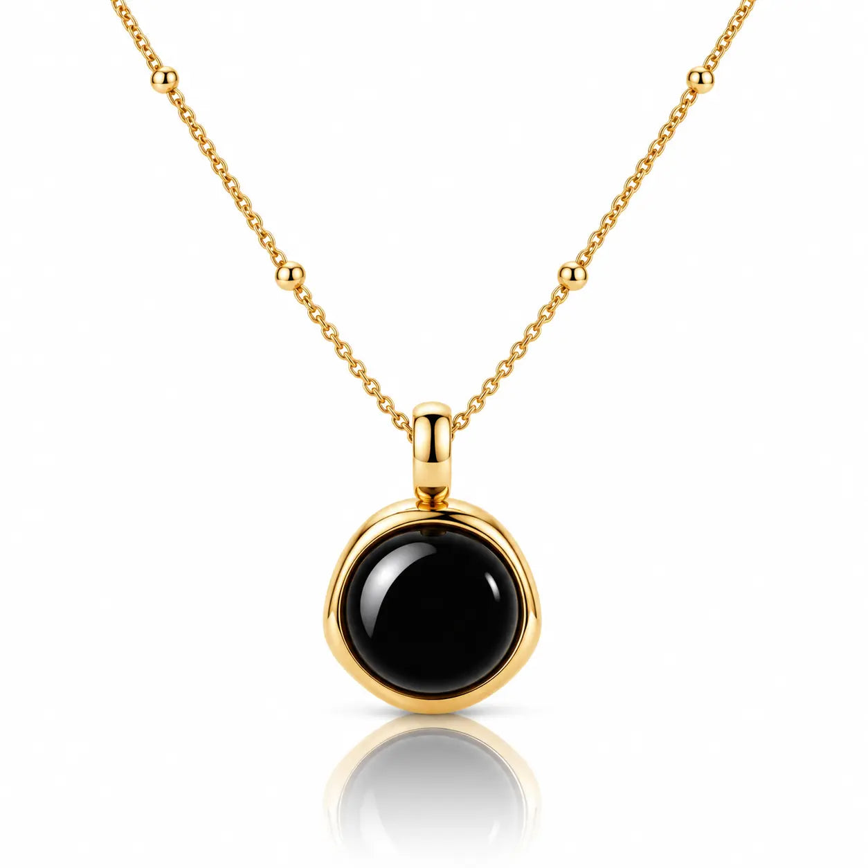 A gold necklace with a round bezel-set black onyx pendant, displayed on a clean white background with a soft reflection below.