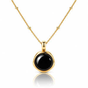 A gold necklace with a round bezel-set black onyx pendant, displayed on a clean white background with a soft reflection below.