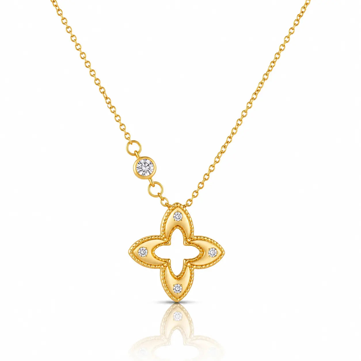 A gold necklace featuring a four-lobed clover or quatrefoil pendant with small clear gemstones set along the edges, suspended from a delicate gold chain with a small round stone accent, shown on a white background with a soft reflection below.