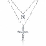 A silver-tone double-strand necklace featuring a small round solitaire pendant and a larger cross pendant paved with small clear stones, shown on a white background.