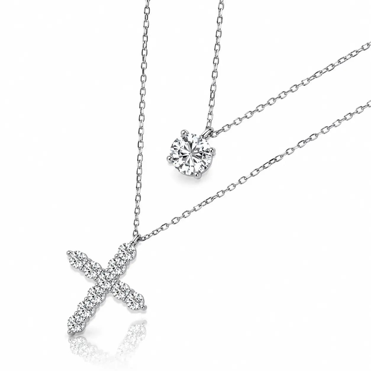 Silver-toned cross pendant necklace and matching solitaire necklace set with clear gemstones, displayed on a clean white background with a soft reflection.