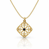 A gold filigree pendant necklace featuring a diamond-shaped openwork design with a central dark blue oval stone and small clear stones, shown on a white background with a soft reflection.