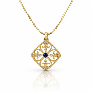 A gold filigree pendant necklace featuring a diamond-shaped openwork design with a central dark blue oval stone and small clear stones, shown on a white background with a soft reflection.