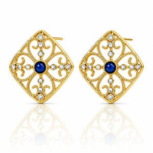 A pair of gold filigree stud earrings with a central deep blue gemstone and small clear rhinestones, displayed on a clean white background with a soft reflection below.