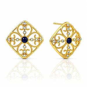 A pair of gold filigree stud earrings with a central dark blue oval stone and small clear round stones, shown on a white background with a soft reflection below.