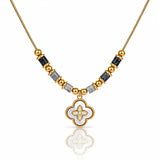 A gold-plated necklace featuring a central white enamel quatrefoil pendant with a gold border, flanked by alternating gold and black faceted beads on a white background.