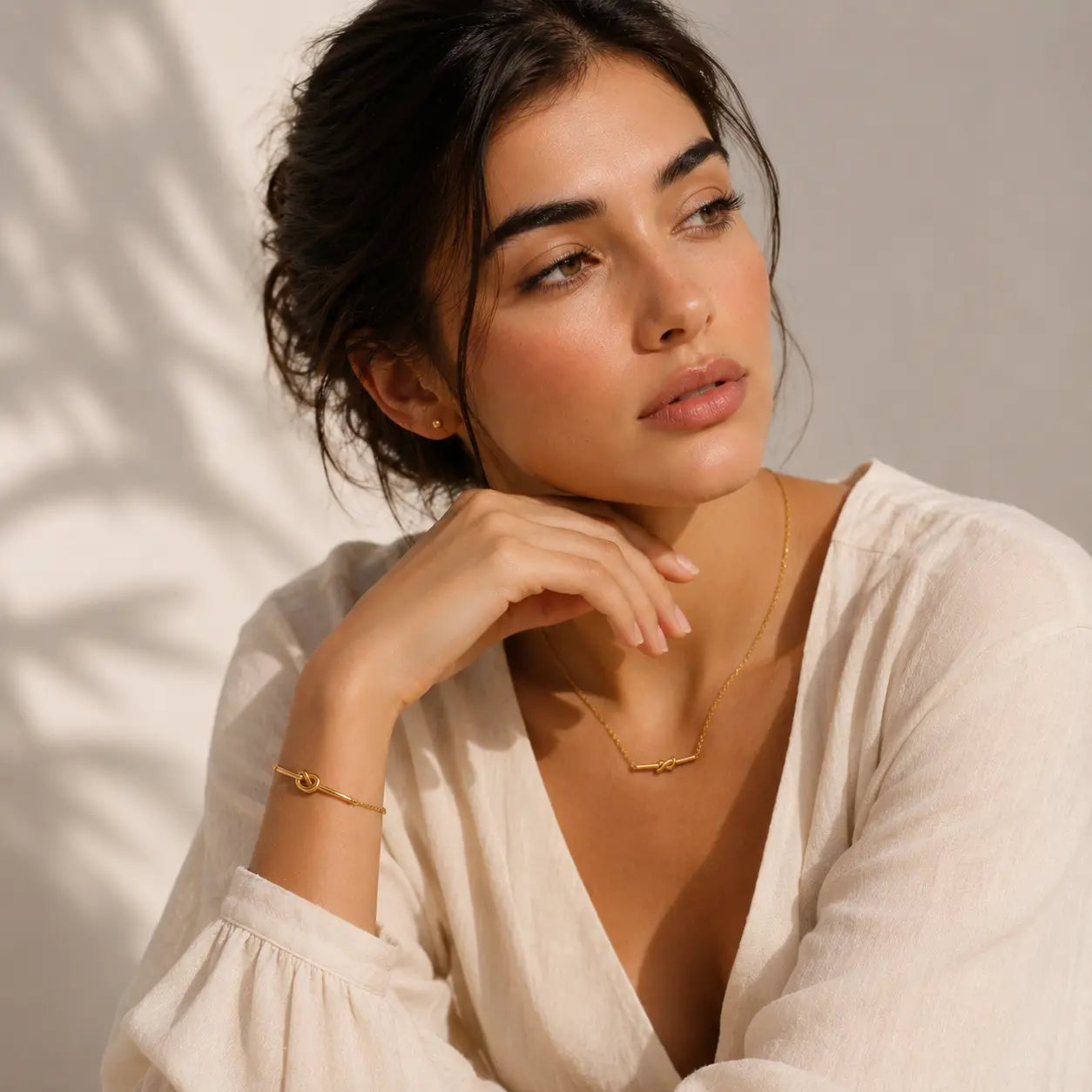 Woman wearing a gold necklace and bracelet against a neutral background