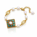 A gold-plated bracelet featuring white baroque pearls, a square gold pendant with turquoise and white pearl details, and leaf-shaped gold links, displayed on a clean white background.